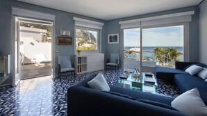A modern living room with a large window overlooking a coastal view, a seating area with a sofa and armchairs, and a patterned floor.
