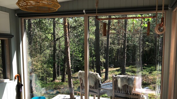 A bedroom with a large bed, a wooden chair, and a view of a forest through a glass door. - Modern Scandinavian family house by forest, lake & 15 mins from Stockholm centre (Saltsjö-boo)
