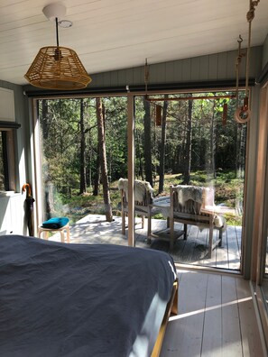 Ein Schlafzimmer mit einem großen Bett, einem hölzernen Stuhl und Blick auf einen Wald durch eine Glastür.