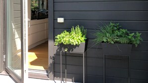 A modern building with a dark exterior, a sliding glass door entrance, and two black planters with green plants on the ground level. - Modern Scandinavian family house by forest, lake & 15 mins from Stockholm centre (Saltsjö-boo)