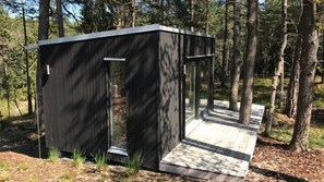 Eine moderne Holz-Blockhütte mit Glastür und einer Holzdielen-Terrasse.