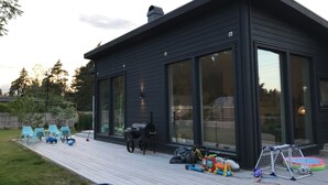 A modern house with large windows, a deck, and outdoor toys. - Modern Scandinavian family house by forest, lake & 15 mins from Stockholm centre (Saltsjö-boo)