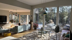 A modern living room with a large TV, comfortable seating, and a view of the outdoors. - Modern Scandinavian family house by forest, lake & 15 mins from Stockholm centre (Saltsjö-boo)