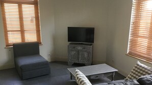 Una sala de estar con un sofá gris, un sillón a juego, una mesa de centro de madera y un televisor sobre un mueble.