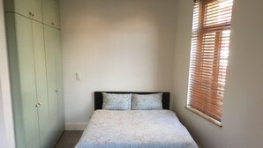 Un dormitorio con cama, armario y ventana con persianas.