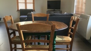 Un comedor con una mesa redonda de madera y seis sillas, un sofá, un televisor y una ventana con persianas.