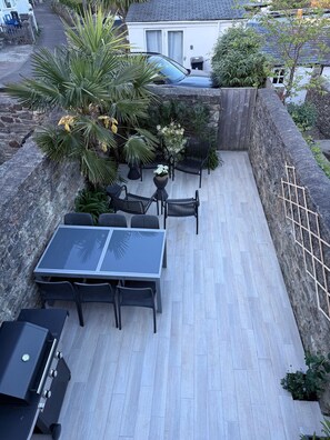 Une terrasse avec une table et des chaises, entourée de plantes et d’un mur en pierre.