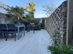 Une terrasse extérieure avec des murs en pierre, une treille en bois et du mobilier d’extérieur.