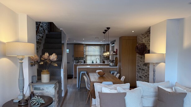 A modern living room with a sofa, dining table, and a kitchen in the background. - Stylish Cottage, central location with harbour view and double parking (Salcombe)