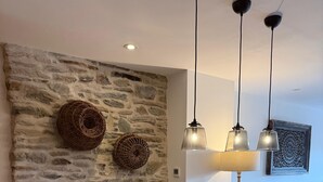 A dining area with a wooden table, white chairs, a stone wall, woven baskets, pendant lights, and a lamp. - Stylish Cottage, central location with harbour view and double parking (Salcombe)