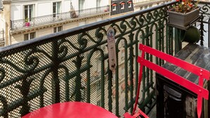Un balcón con barandilla de hierro forjado, con vistas a un paisaje urbano que incluye edificios históricos y una torre a lo lejos.