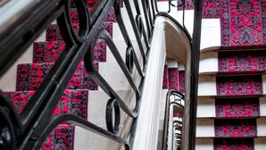 Una escalera con barandillas de metal negro y un suelo de alfombra estampada.