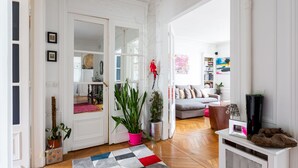 Un salón amplio con suelo de madera, alfombra de cuadros, sofá gris y televisor sobre un mueble blanco.