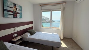 Ein Schlafzimmer mit zwei Betten, einem Fenster mit Meerblick, einem Bild an der Wand und einer Klimaanlage.