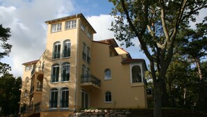 A multi-story building with a yellow facade, multiple balconies, and a stone retaining wall in the foreground.