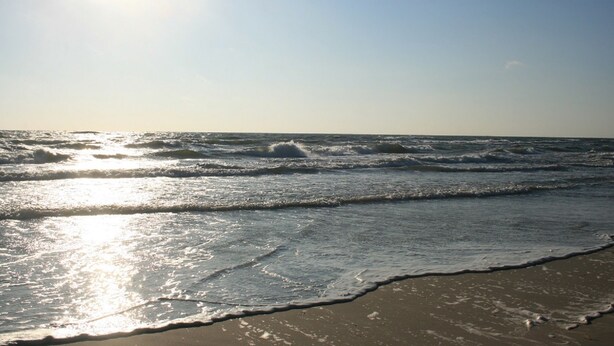 A beach with waves and sunlight reflecting on the sand.