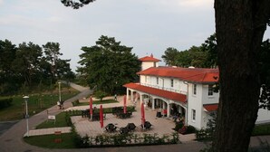 A white building with a red roof, surrounded by trees and a paved area with outdoor seating.