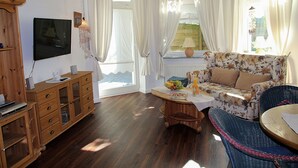 A living room with a wooden cabinet, a television, a floral sofa, a wicker chair, and a table with a lamp.