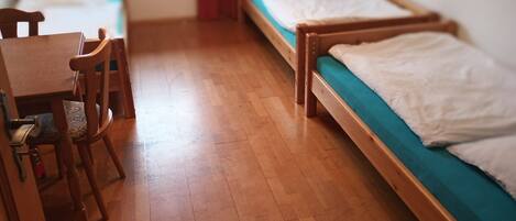 A dormitory room with wooden furniture, including a desk and chairs, and two single beds with teal bedding.