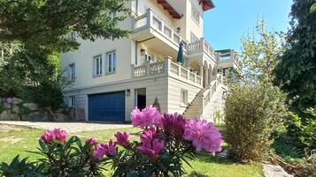 Ein mehrstöckiges Gebäude mit Balkon, Garage und einem gepflegten Garten mit rosa Blüten.