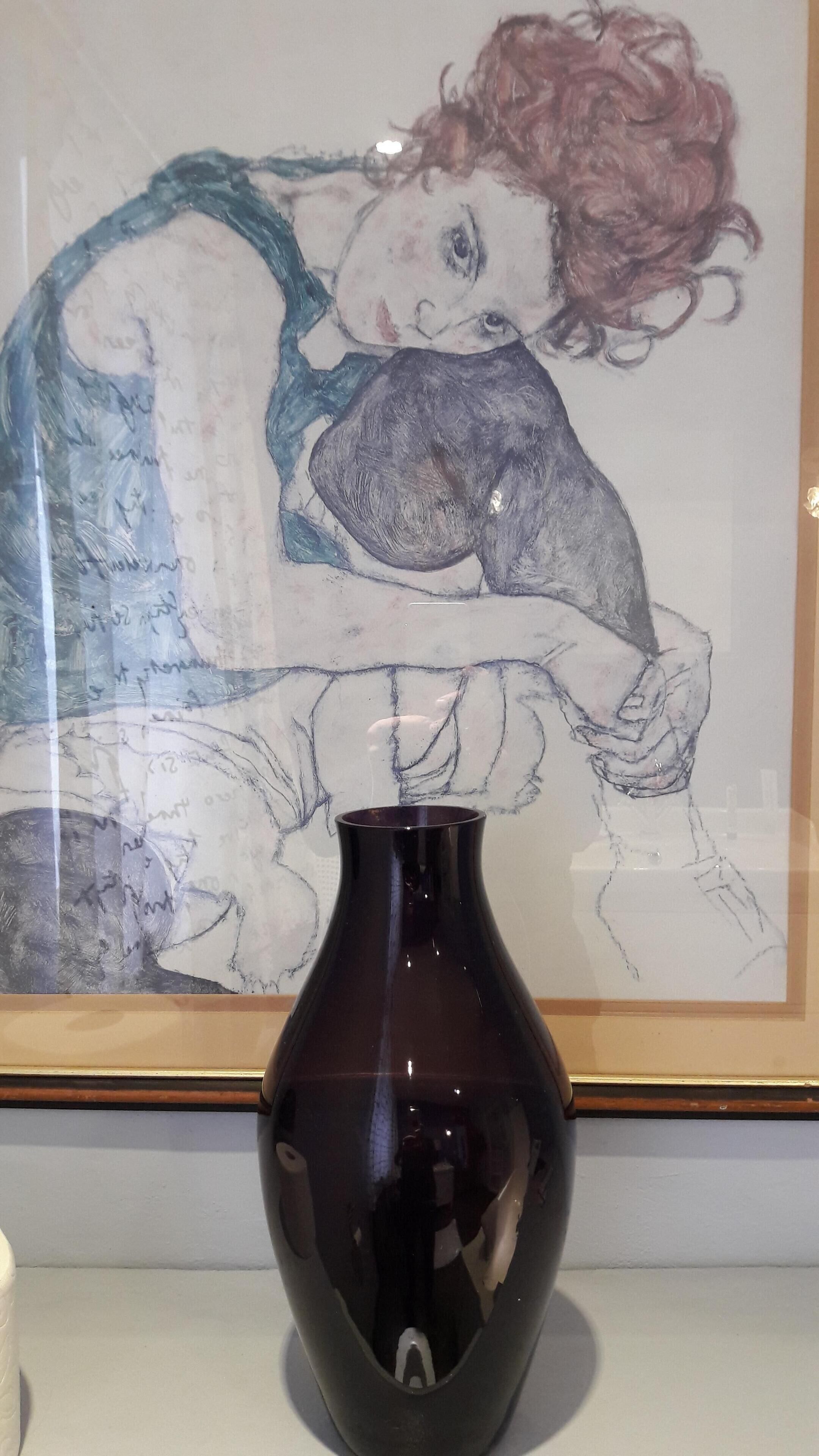 Een lijstwerk met een afbeelding van een uitgestrekt liggend figuur met krullen, een donkere vaas op de voorgrond, en een houten lijst.