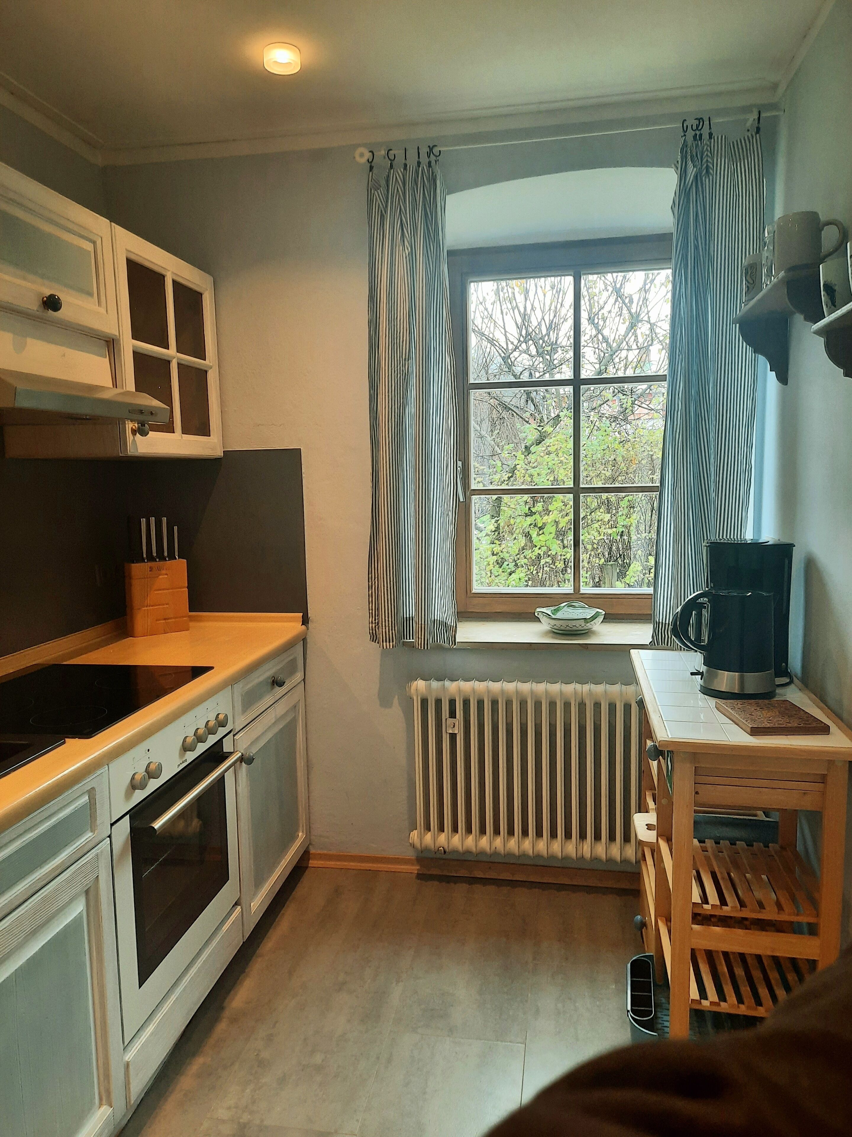 A compact kitchen with white cabinets, a stove, oven, and a window with curtains.