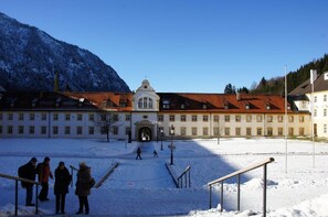 A large building with a central entrance, surrounded by snow-covered ground and mountains in the background.