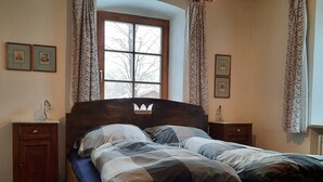 A wooden bed with a headboard, flanked by two nightstands, in a room with wooden floors and a sloped ceiling. - King Ludwig' a fairytale apartment (Oberammergau)