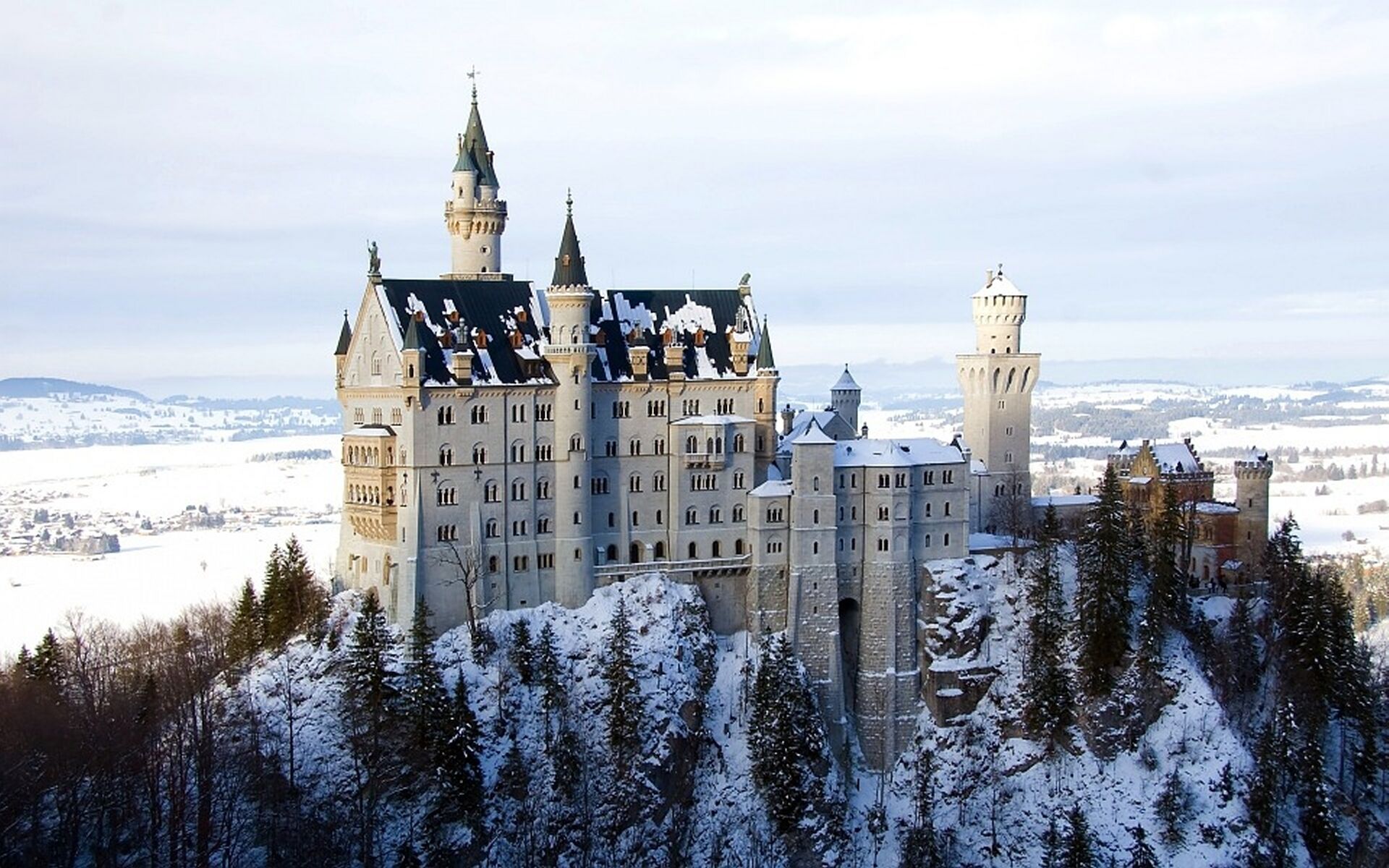 Ein großes, historisches Schloss mit mehreren Türmen und einem markanten Hauptgebäude, umgeben von schneebedeckten Bäumen und einer Winterlandschaft.
