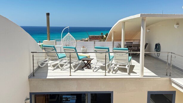 A sun deck with lounge chairs and a table, overlooking the ocean. - Villa Bianca, with its own pool and Wi-Fi, close to the ocean, sheltered courtyard (patio) (Costa Calma)