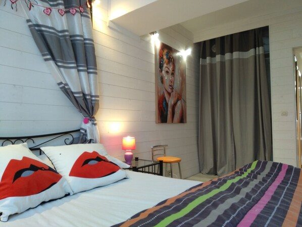 A hotel room with a bed, a bedside table with a lamp, a chair, and a painting on the wall.