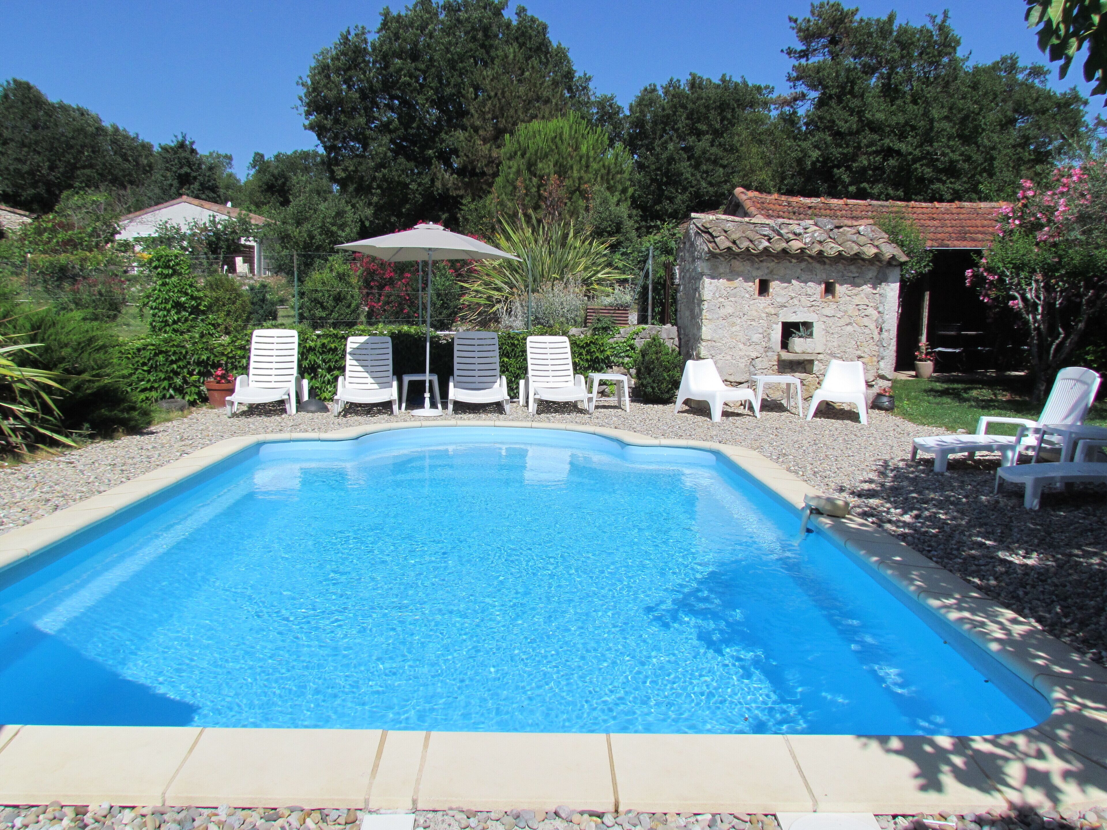 A rectangular swimming pool with clear blue water, surrounded by white lounge chairs and a stone building in the background.