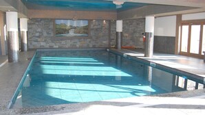 An indoor swimming pool with stone walls and a mural, large windows, and a tiled floor. - Arc 1800 Iseran, ski-in ski-out, heated swimming pool, cleaning included (Bourg-Saint-Maurice)