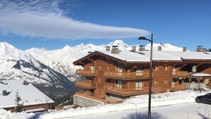 A wooden chalet with balconies and a snow-covered roof, surrounded by mountains. - Arc 1800 Iseran, ski-in ski-out, heated swimming pool, cleaning included (Bourg-Saint-Maurice)