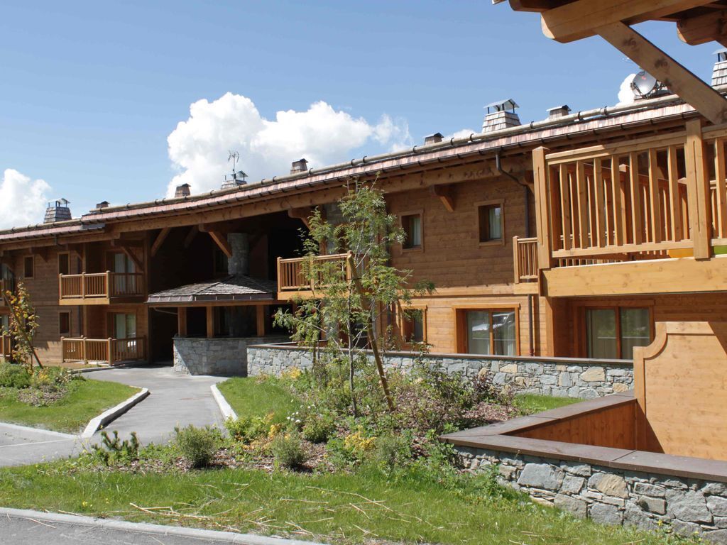 A multi-story wooden building with balconies, a stone foundation, and a clear sky.