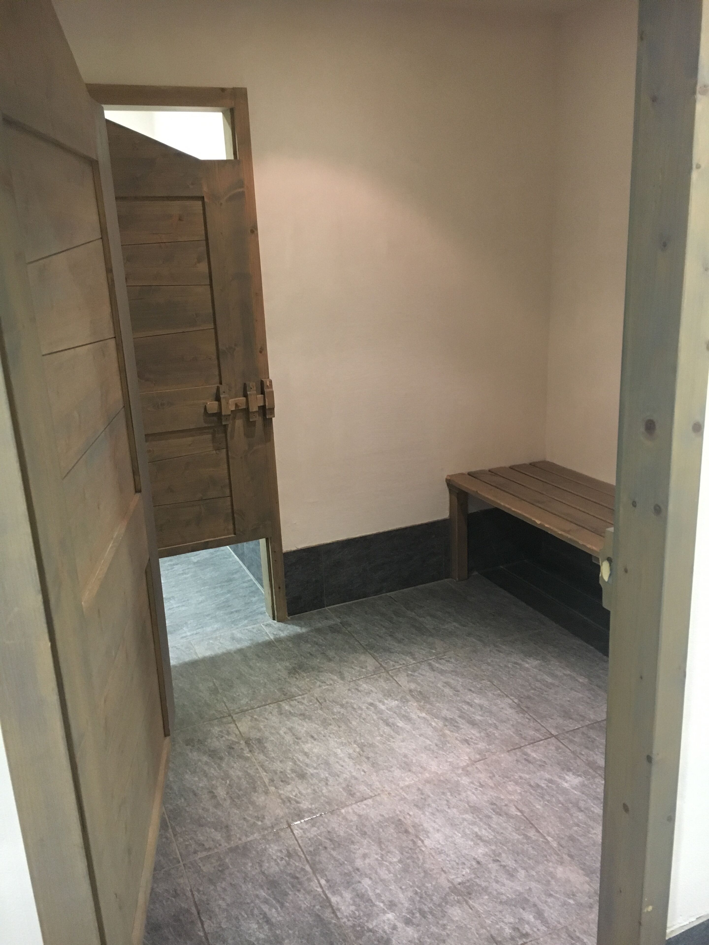 A small room with a wooden door, a bench, and tiled flooring.