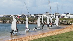 Un port de plaisance où plusieurs voiliers sont amarrés et où des personnes pratiquent diverses activités nautiques.