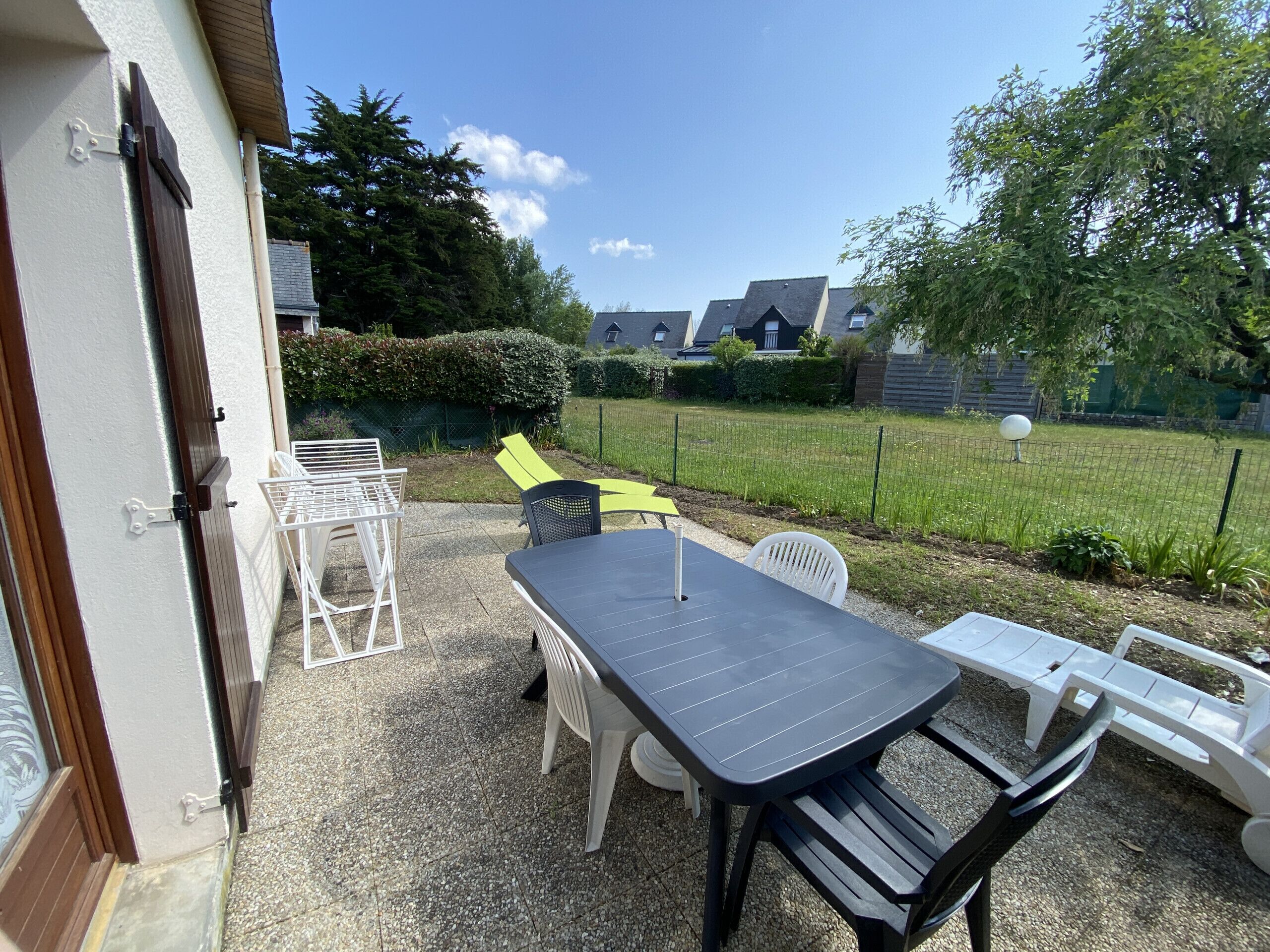 A patio area with a table and chairs, a door, and a view of a grassy yard and houses in the background.