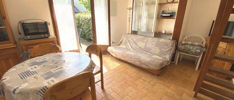 A compact room with a dining table, chairs, a sofa, a television, and a sliding door leading to a garden.