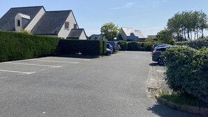 A parking lot with cars parked, a hedge, and houses in the background. - CLOS DUNES - Jardin, Piscine partagée - ED6019 (Erdeven)