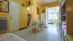 A room with a bed, a chair, a table, a refrigerator, and a window with curtains.