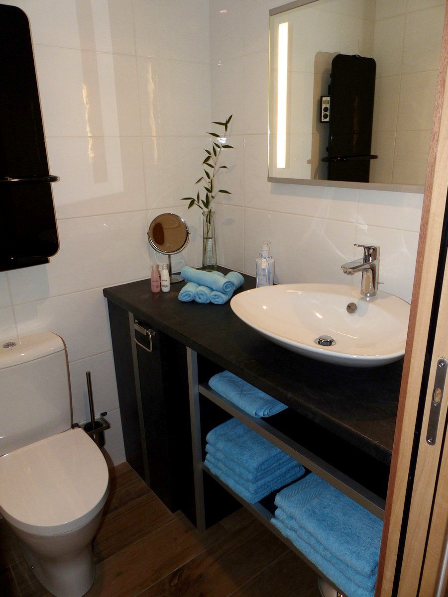 A modern bathroom with a white toilet, a sink with a mirror above it, and a towel rack with folded towels.