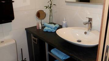 A modern bathroom with a white toilet, a sink with a mirror above it, and a towel rack with folded towels.