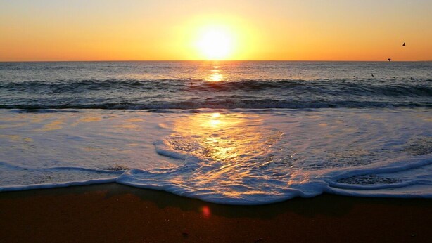 Una spiaggia al tramonto con le onde che lambiscono dolcemente la riva.