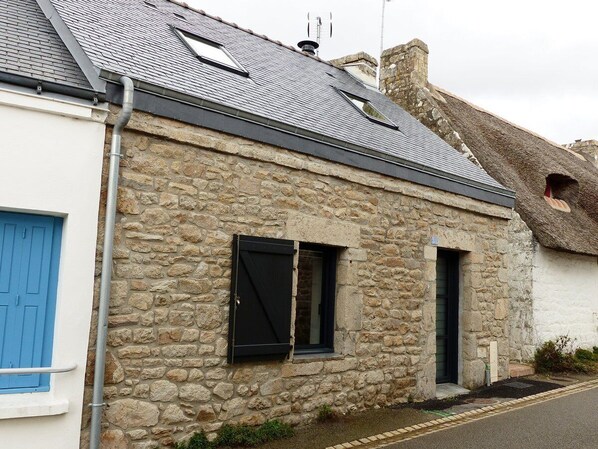 A stone building with a thatched roof, a blue door, and a small window with a shutter.