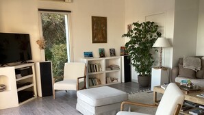 Un salon moderne doté d’un téléviseur à écran plat, d’une bibliothèque, d’une grande plante en pot et d’un coin salon confortable.