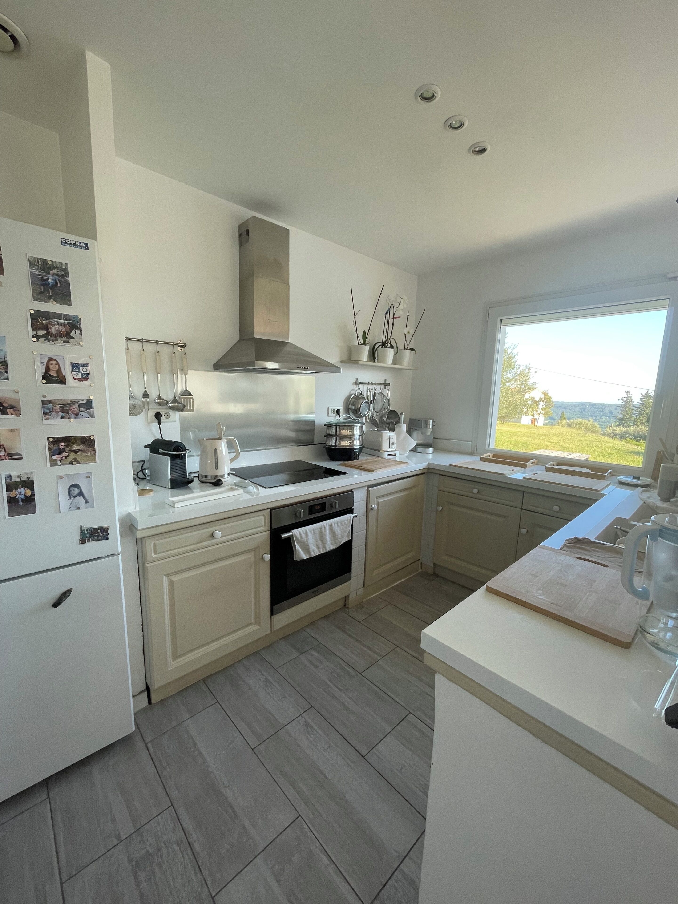A modern kitchen with a built-in oven, stainless steel range hood, and a large window offering a view of the outdoors.