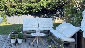 Une terrasse en bois avec un coin salon doté de coussins blancs et une petite table ronde.