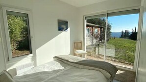 Une chambre à coucher avec un lit, une chaise et une vue sur l’extérieur grâce à de grandes fenêtres.