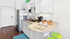 Une cuisine compacte avec des meubles blancs, un four à micro-ondes, une machine à café et un petit îlot central doté de tabourets.